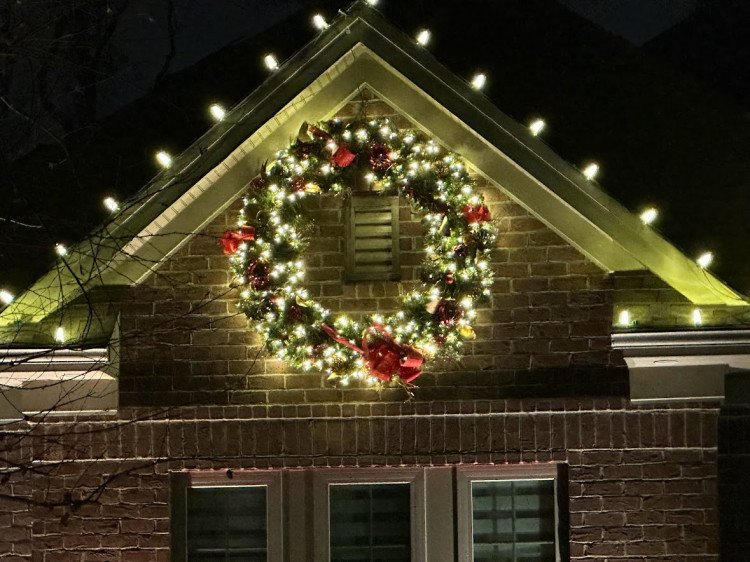 Large Christmas wreath with warm white lights hung on a brick front gable by Lights Around