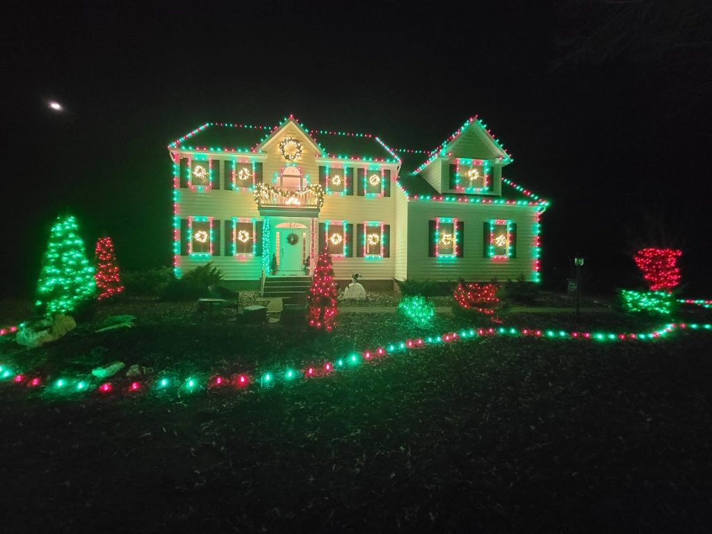Custom residential Christmas light installation featuring warm white LED roofline and entryway lighting on a two-story suburban home at night.