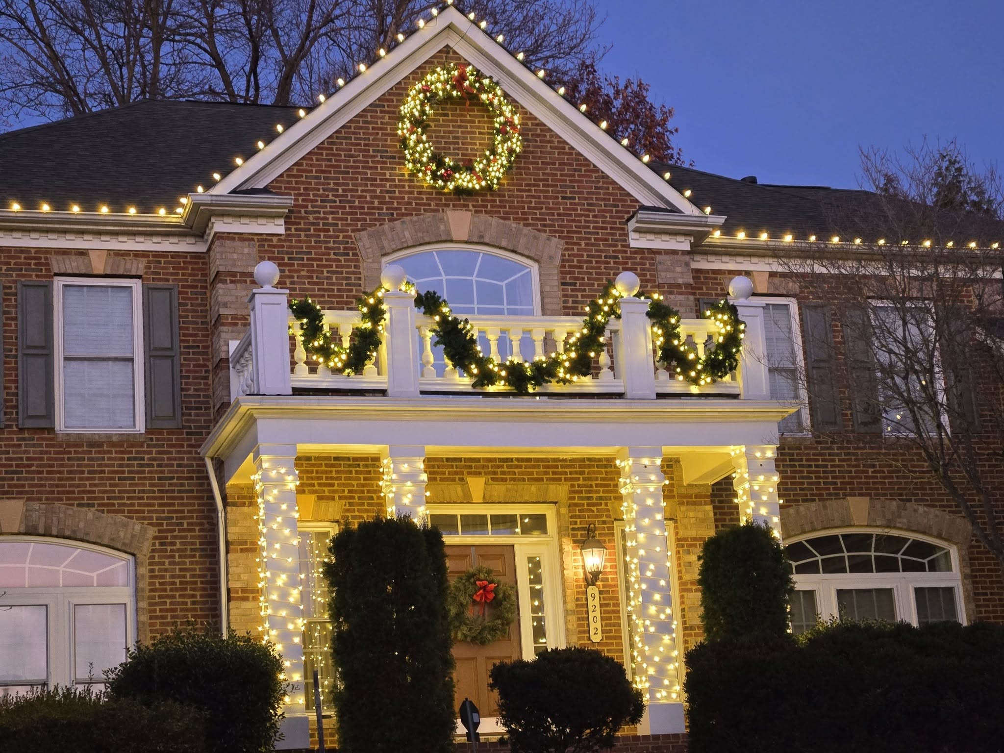 Professionally installed Christmas lights outlining the roofline and porch of a brick home