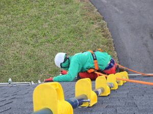 Professional Christmas light installer sitting on a rooftop ridge wearing safety harness gear
