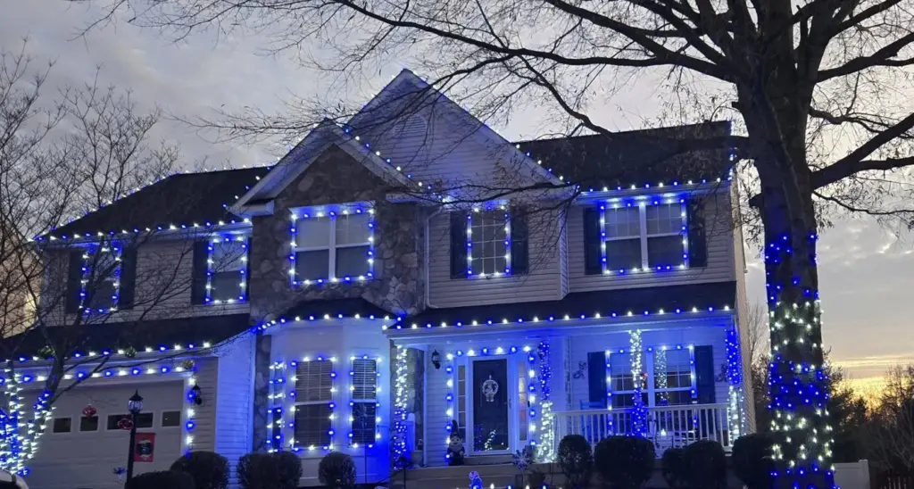 Blue and white Christmas lights on a roofline, windows and a wrapped tree