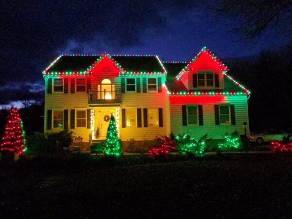 Two-story house at night brightly illuminated with vibrant, multi-colored red, green, and yellow Christmas lights along the roofline and landscaping in Richmond Area.